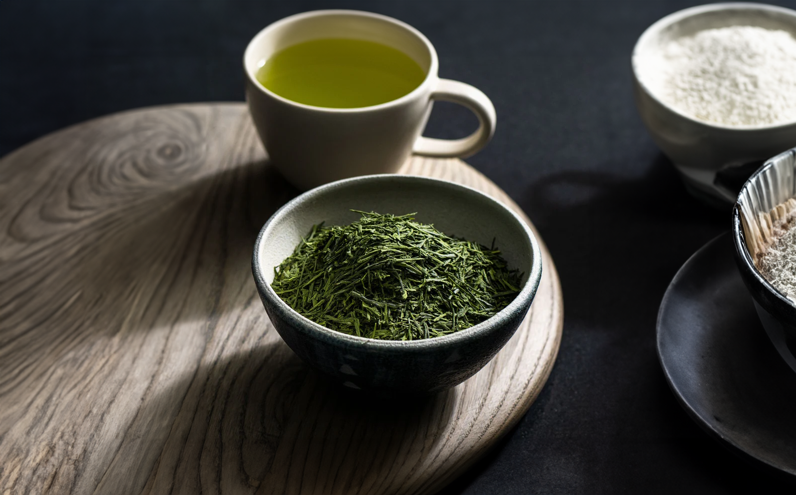 Thé vert Gyokuro bio en feuilles entières dans un bol en céramique, avec tasse de thé infusé à l’arrière-plan.